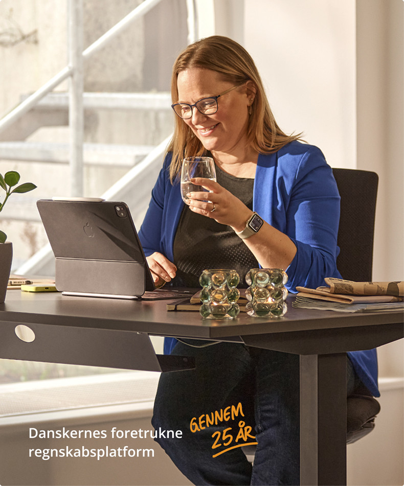 En kvinde sidder ved en computer med et glas vand i hånden